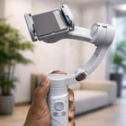 Hand holding a smartphone gimbal stabilizer in a blurred indoor setting
