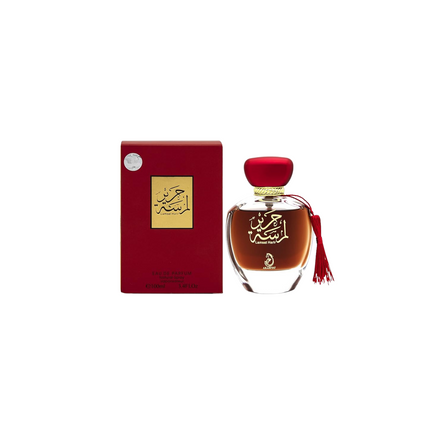 Perfume bottle with red cap and tassel next to its packaging on a white background