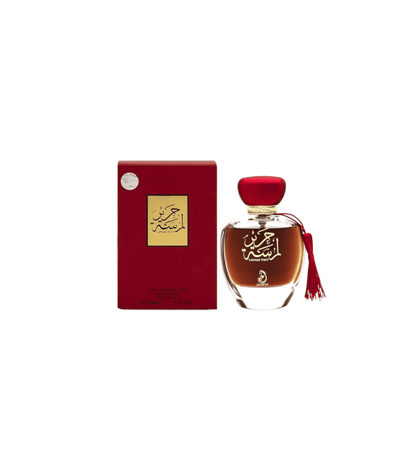 Perfume bottle with red cap and tassel next to its packaging on a white background