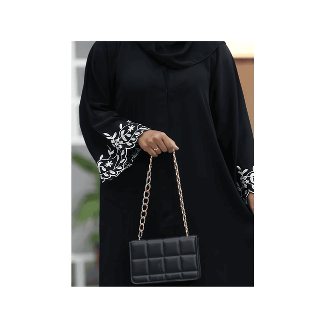 Person wearing a black outfit with white patterns, holding a black handbag with gold chain strap.