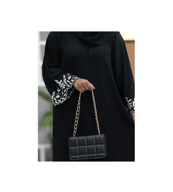 Person wearing a black outfit with white patterns, holding a black handbag with gold chain strap.