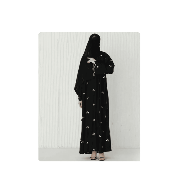 Person wearing a black abaya with floral embroidery on a white background