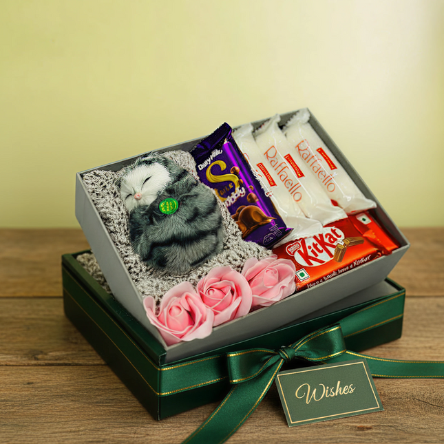 Gift set with plush toy, chocolate bars, and flowers in a decorative box on a wooden surface.