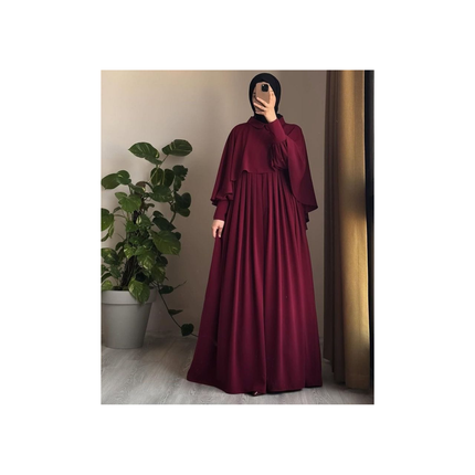 Person wearing a burgundy dress standing in front of a plant.