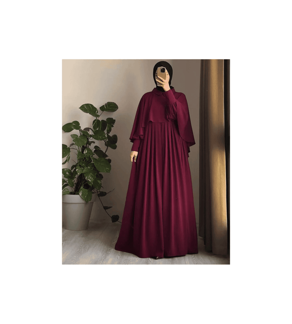 Person wearing a burgundy dress standing in front of a plant.