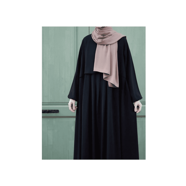 Person wearing a black outfit with a pink hijab against a green door background