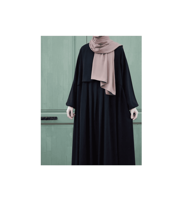 Person wearing a black outfit with a pink hijab against a green door background