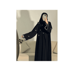 Person wearing a black abaya with white details in a neutral setting