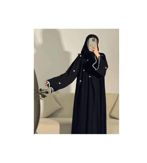 Person wearing a black abaya with white details in a neutral setting