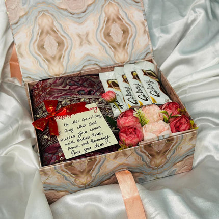 Gift box with flowers, cards, and a ring on a white satin surface