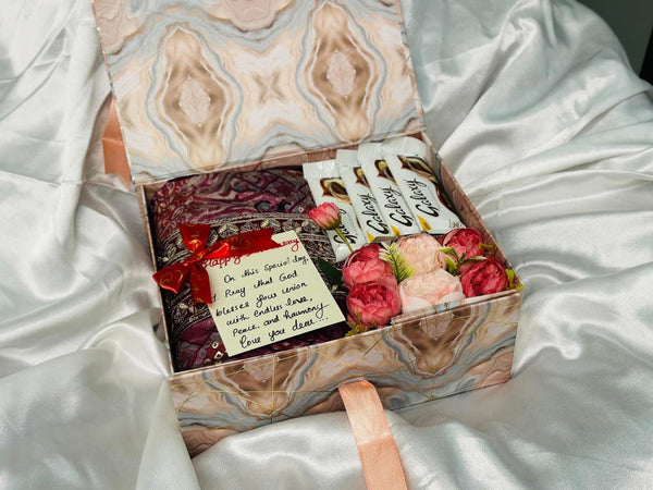Gift box with flowers, cards, and a ring on a white satin surface