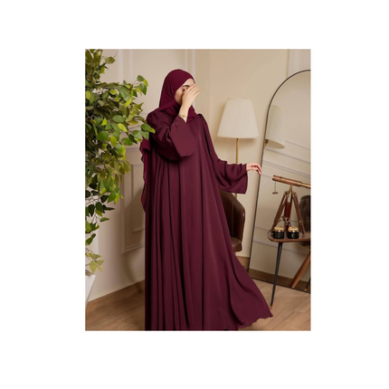 Woman wearing a burgundy abaya in a room with a lamp and plant.