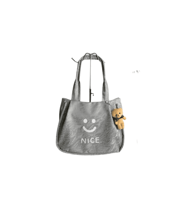 Gray tote bag with a smiley face and 'NICE' text, containing a small teddy bear, on a white background.