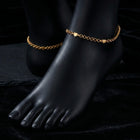Gold anklets on a black foot mannequin against a dark background