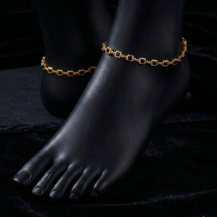 Gold anklets on a black foot mannequin against a dark background