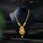 Gold necklace on a black mannequin bust against a dark background