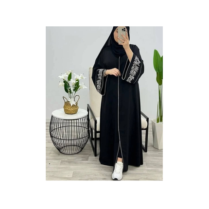 Person wearing a black abaya with white embroidery in a minimalistic room.