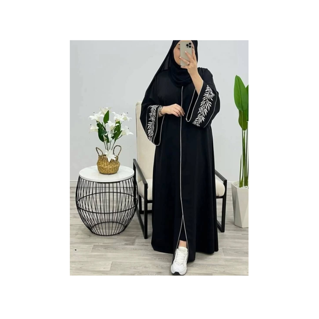 Person wearing a black abaya with white embroidery in a minimalistic room.