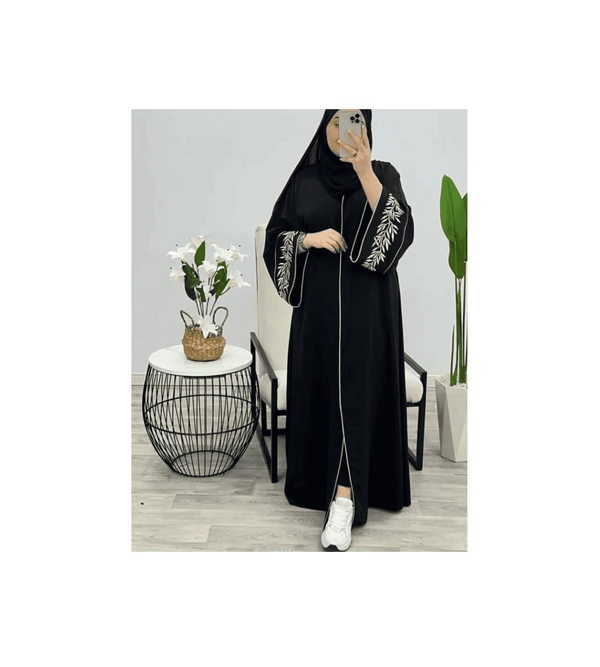 Person wearing a black abaya with white embroidery in a minimalistic room.